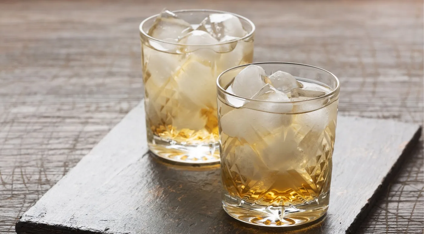 Two glasses of Irish whiskey over ice on a rustic wooden board