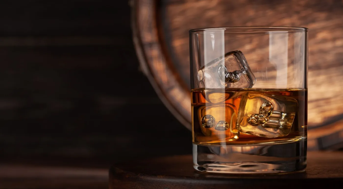 A glass of Irish whiskey on the rocks glowing beside an oak maturing barrel